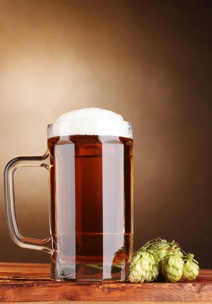 Chmiel kubek i zielone piwo na drewnianym stole na brązowym tle — Zdjęcie stockowe