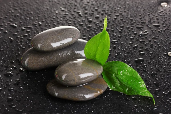 Wellness-Steine mit Wassertropfen und Blättern auf schwarzem Hintergrund — Stockfoto