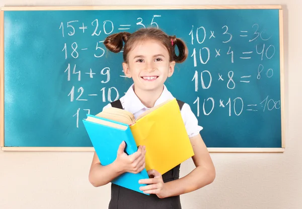Güzel küçük bir kız sınıfta blackboard yakın duran kitaplar — Stok fotoğraf