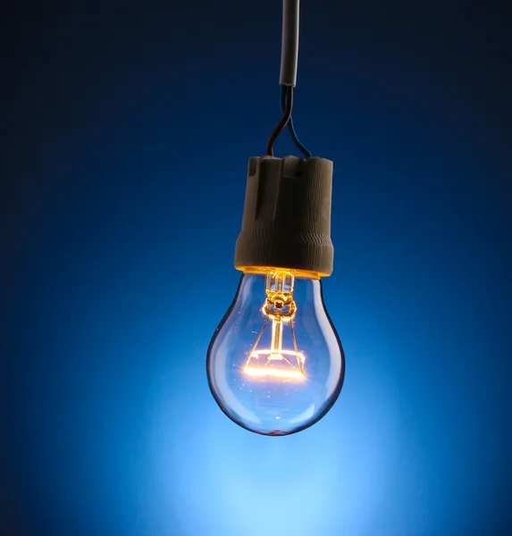 Uma lâmpada acesa no fundo azul — Fotografia de Stock
