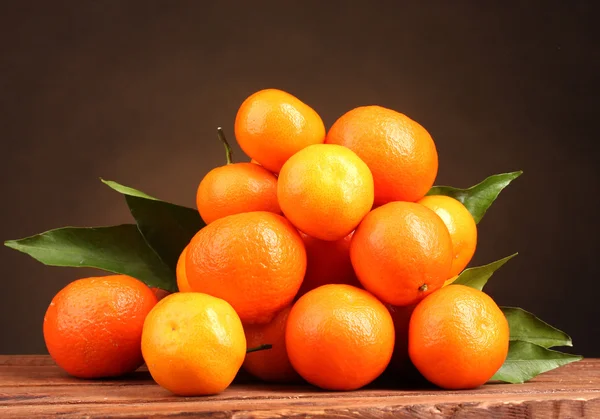 Tangerines met bladeren op houten tafel op bruine ondergrond — Stockfoto