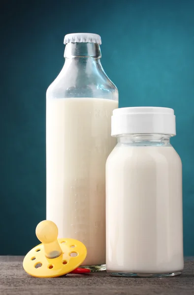 Butelki mleka i smoczek na drewnianym stole na niebieskim tle — Zdjęcie stockowe