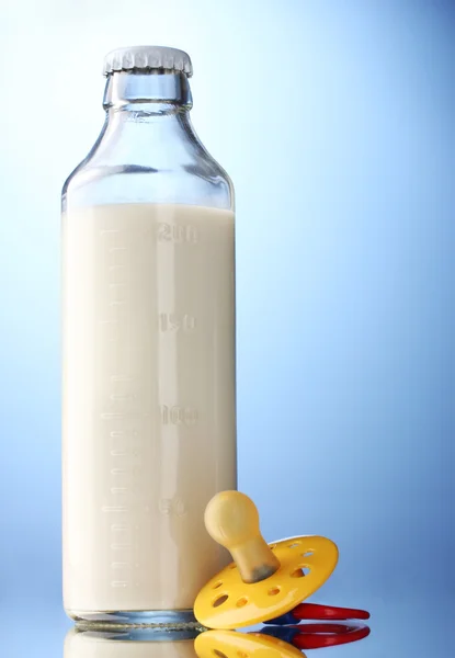 Butelka mleka i smoczek na niebieskim tle — Zdjęcie stockowe
