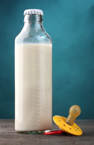 Бутылка молока и успокаивающее на деревянном столе на голубом фоне — стоковое фото