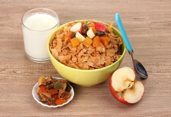 Tasty cornflakes in bowl with dried fruits, glass of milk and apple on wood — Stock Photo, Image