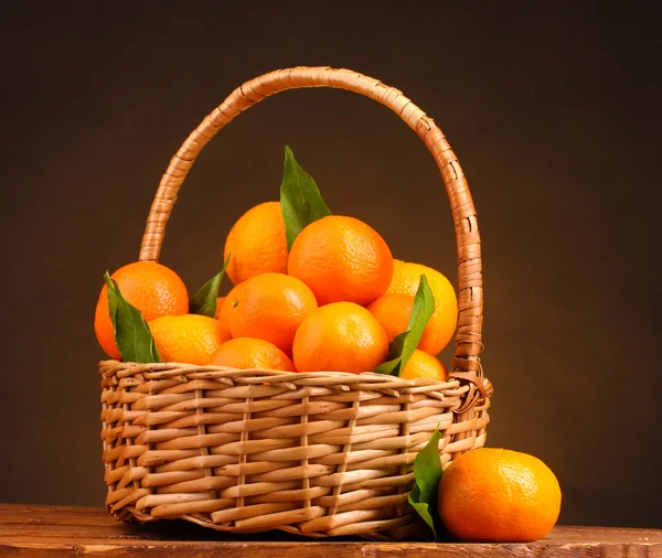 Tangerines with leaves in a beautiful basket on wooden table on brown backg Stock Picture
