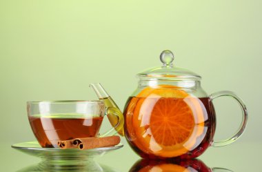 Black exotic fruit tea in glass teapot and cup on green background clipart