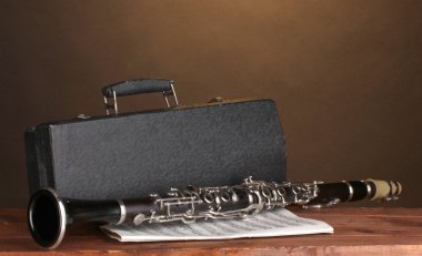 Old clarinet, case and notebook with notes on wooden table on brown backgro clipart