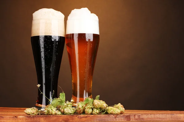 Heupferdzwarte en gouden bier in glazen en hop op houten tafel op bruin pagina — Stockfoto