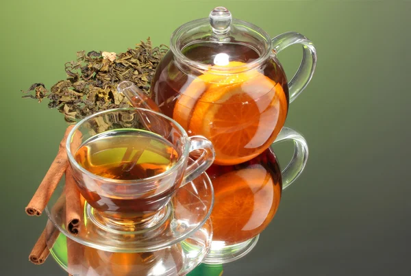 stock image Black exotic fruit tea in glass teapot and cup on green background