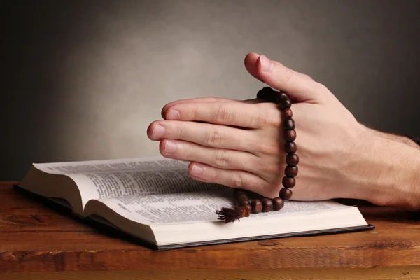 Mãos segurando rosário de madeira sobre bíblia santa russa aberta sobre fundo cinza — Fotografia de Stock