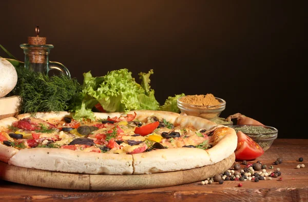 Vynikající pizza, zelenina a koření na dřevěný stůl na hnědé pozadí — Stock fotografie