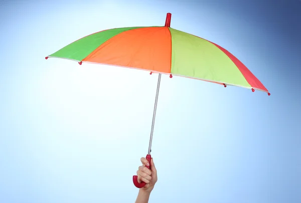 Mehrfarbiger Regenschirm in der Hand auf blauem Hintergrund — Stockfoto
