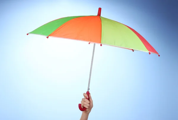 Multi-colored umbrella in hand on blue background — Stock Photo, Image