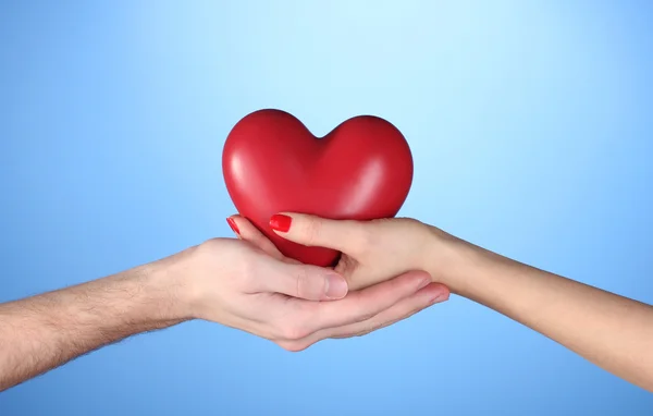 Мужчина и женщина держат в руках красное сердце на синем фоне — стоковое фото