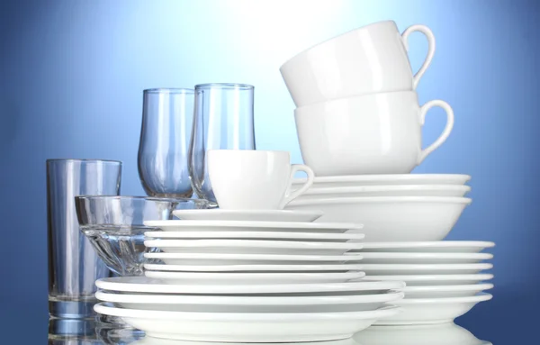 Puste miski, talerze, kubki i szklanki na niebieskim tle — Zdjęcie stockowe