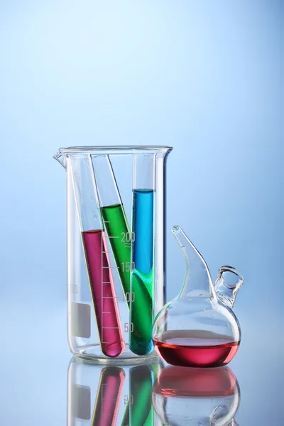 Artículos de vidrio de laboratorio con líquido de color y con reflexión sobre el fondo azul —  Fotos de Stock