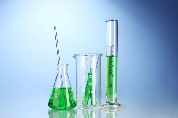 Laborgläser mit grüner Flüssigkeit mit Reflexion auf blauem Hintergrund — Stockfoto