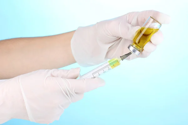 Syringe and medical ampoule in hands on blue background — Stock Photo, Image