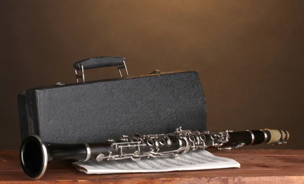 Antiguo clarinete, estuche y cuaderno con notas sobre mesa de madera sobre fondo marrón — Foto de Stock