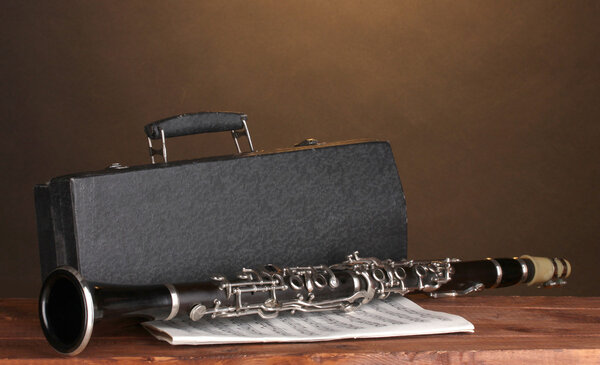 Old clarinet, case and notebook with notes on wooden table on brown backgro