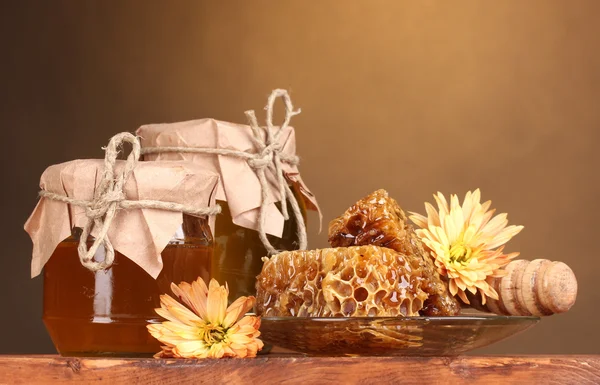 Dos tarros de miel, panales de miel y llovizna de madera en la mesa sobre fondo amarillo — Foto de Stock
