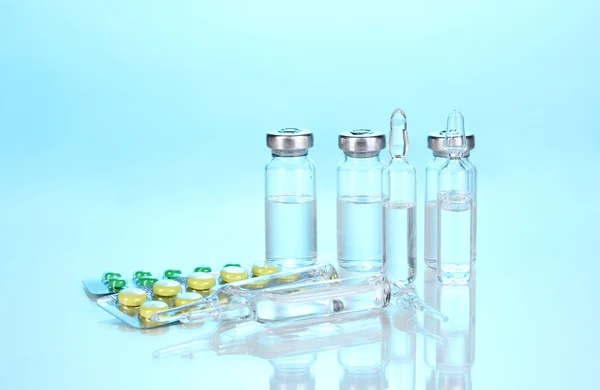 Jeringa con ampollas y tabletas médicas sobre fondo azul — Foto de Stock