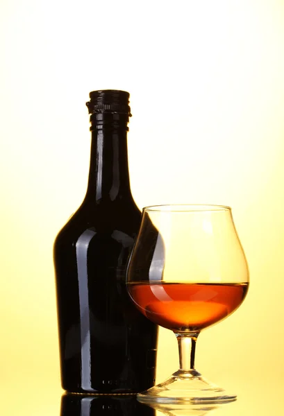 Vaso de brandy y botella sobre fondo amarillo —  Fotos de Stock