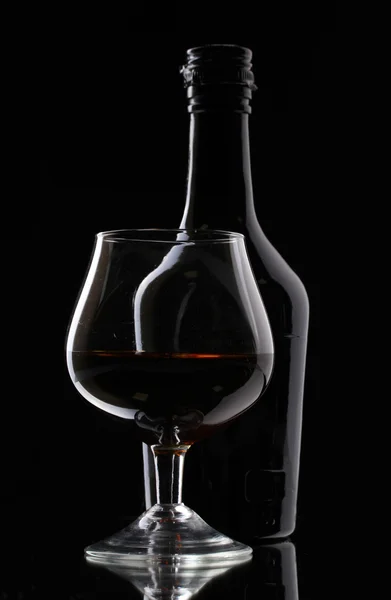 Vaso de brandy y botella sobre fondo negro — Foto de Stock