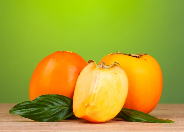 Appetizing persimmons on wooden table on green background — Stock Photo, Image