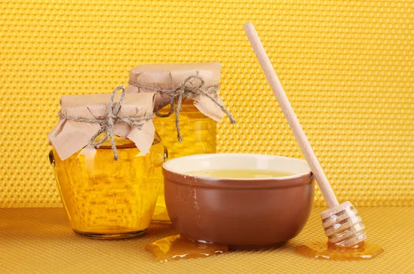 Jars of honey, bowl and wooden drizzler with honey on yellow honeycomb back Stock Photo