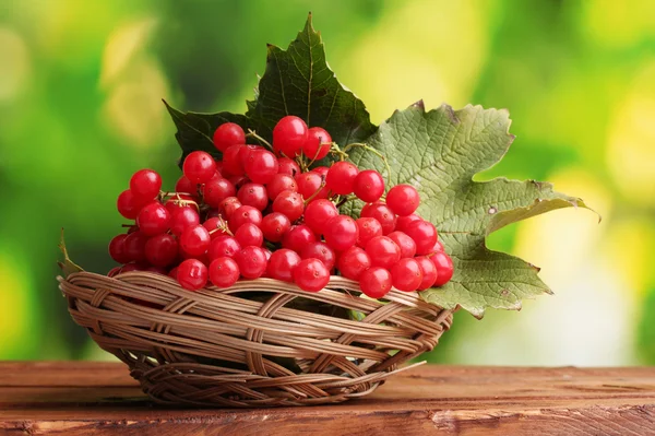 Красные ягоды вибурнума в корзине на деревянном столе на зеленом фоне — стоковое фото