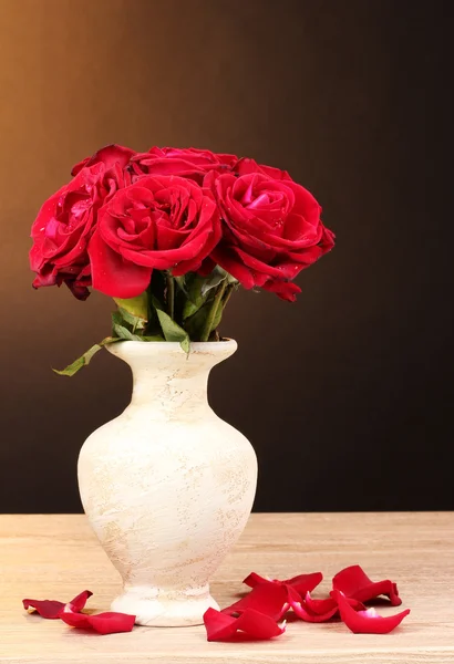 Mooie rode rozen in vaas op houten tafel op bruine achtergrond — Stockfoto