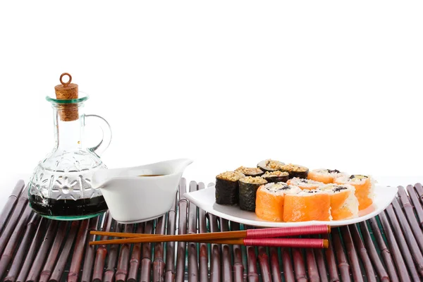 Leckere Brötchen auf weißem Teller serviert mit Stäbchen und Sojasauce auf Bambus m — Stockfoto