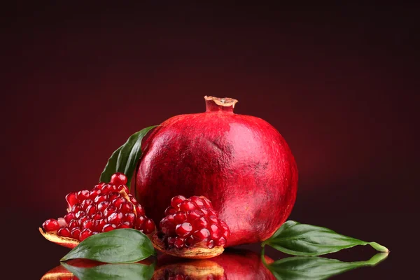 Fruta de granada madura con hojas sobre fondo rojo —  Fotos de Stock