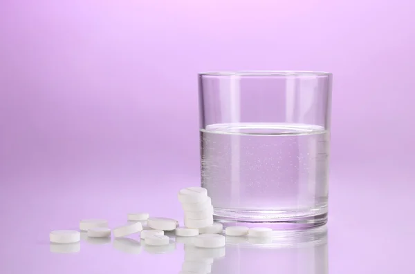 Glass of water and pills on purple background — Stock Photo, Image