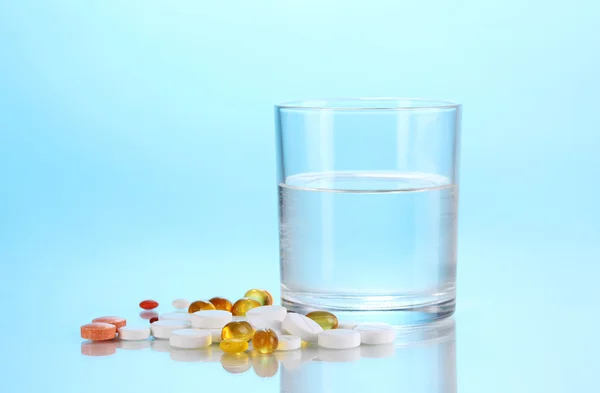 Склянка води і таблетки на синьому фоні — стокове фото
