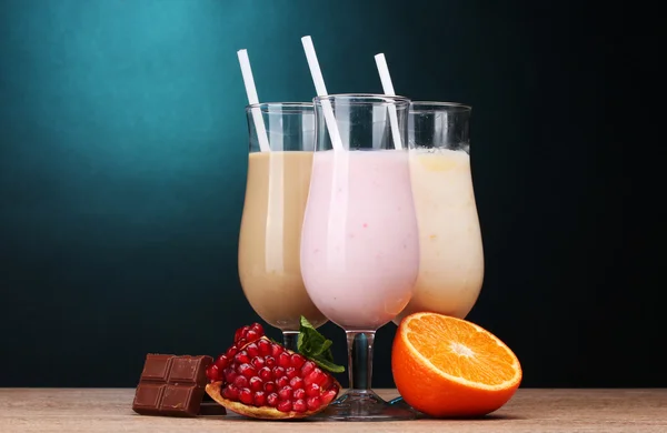 Milk shakes with fruits and chocolate on wooden table on blue background — Stock Photo, Image
