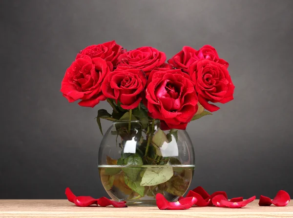 Beautiful red roses in vase on wooden table on gray background — Stock Photo, Image