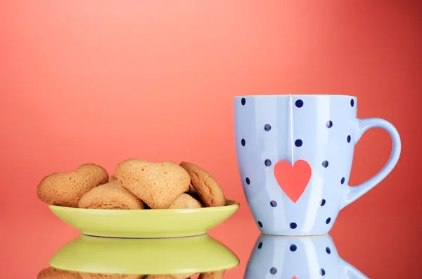 Heart-shaped cookies on plate and cup with tea bag on red background — Stock Photo, Image