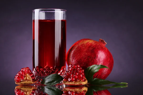 stock image Ripe pomergranate and glass of juice on purple background