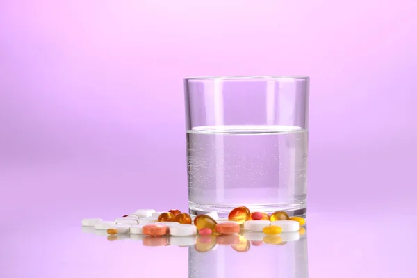 Glas water en pillen op paarse achtergrond — Stockfoto