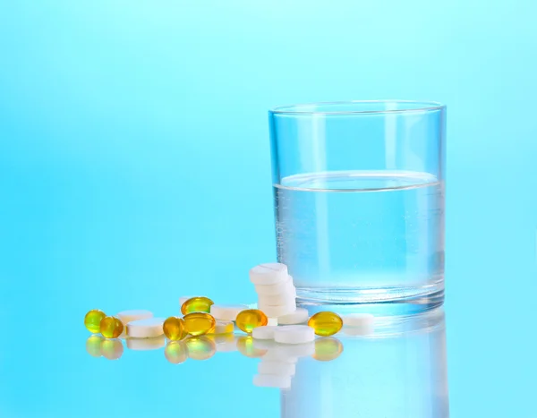 Glass of water and pills on blue background — Stock Photo, Image