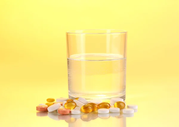Glass of water and pills on yellow background — Stock Photo, Image