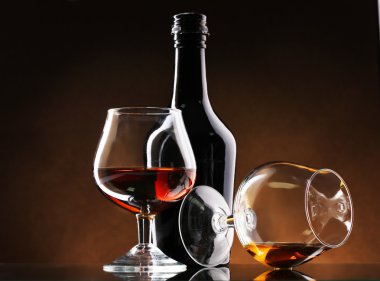 Glasses of brandy and bottle on brown background clipart