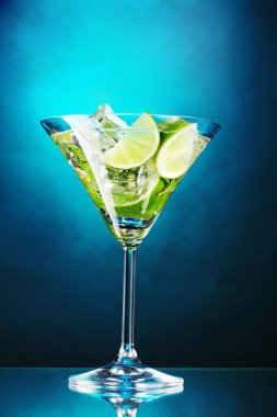 Glass of cocktail with lime and mint on blue background clipart