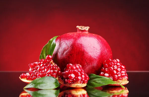 Fruta de romã madura com folhas no fundo vermelho — Fotografia de Stock