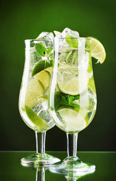 Glasses of cocktails with lime and mint on green background — Stock Photo, Image
