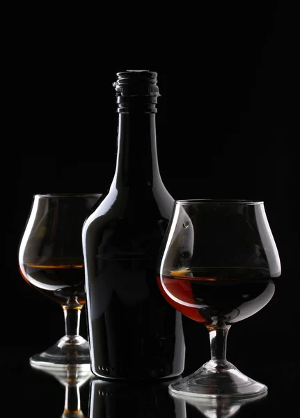 Óculos de conhaque e garrafa sobre fundo preto — Fotografia de Stock