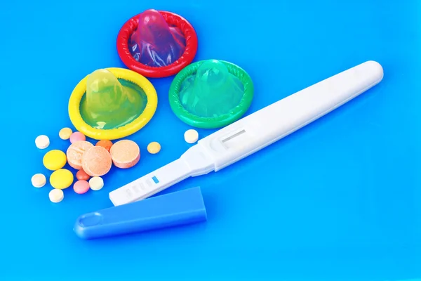 Презервативы, тест на беременность и контрольные таблетки на синем фоне — стоковое фото